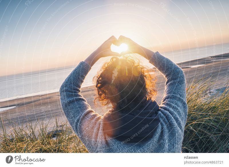 Girl holding a heart-shape with sunset light on the beach woman hand lifestyle travel love harmony curls concept sunlight dawn symbol shaped adventure baltic