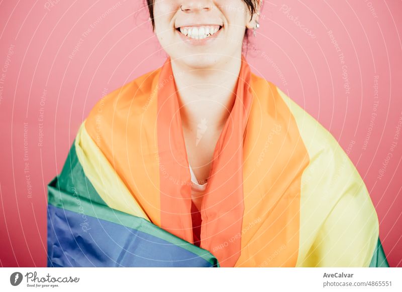 Woman smiling happily to camera while holding a LGBTIQ flag around her showing pride. Lesbian woman, pride and fighting for her rights. Love is love concept. Color background image
