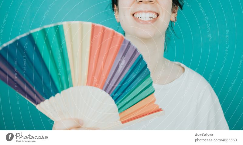 Woman smiling happily to camera while holding a LGBTIQ hand fan her showing pride. Lesbian woman, pride and fighting for her rights. Love is love concept. Color background image