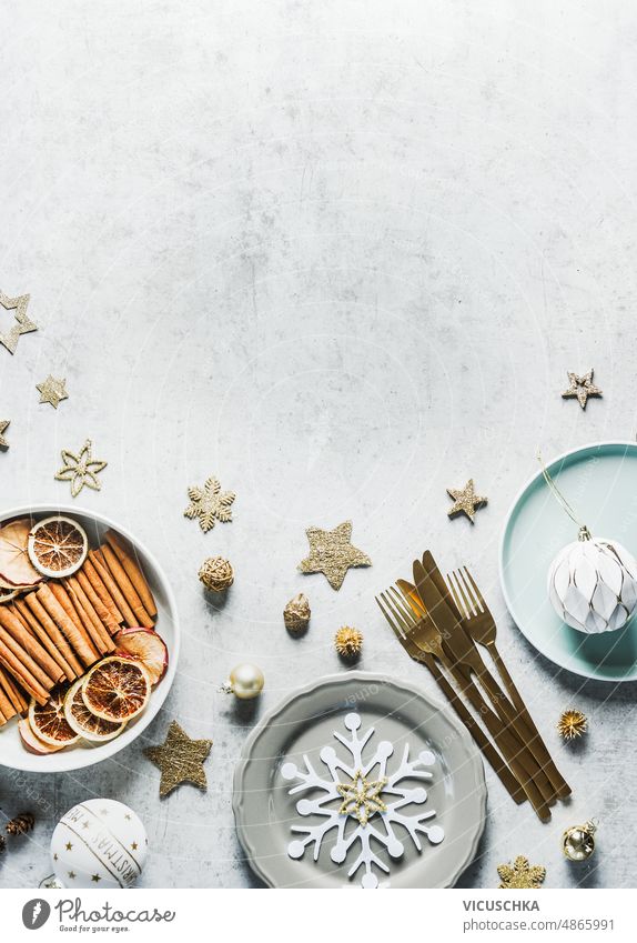 Christmas background with table setting, plates, golden cutlery, decoration and fir green, snow and cinnamon sticks, baubles at concrete backdrop. Festive dinner background.