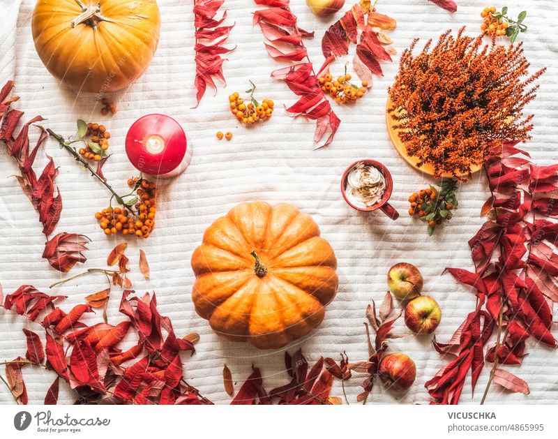 Autumn flat lay composition with pumpkins, red and orange leaves, candle, hot chocolate with cream, apples at white textile background. autumn cozy seasonal
