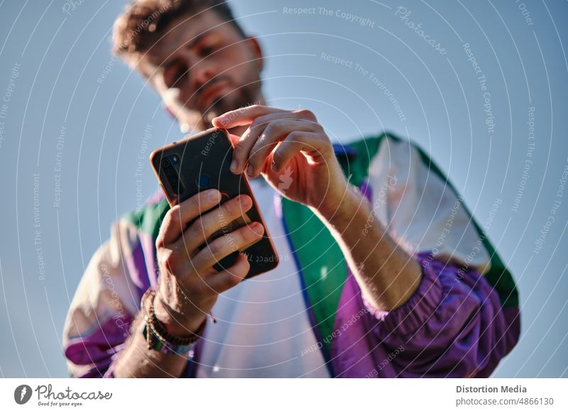 Young man looking at his mobile phone seen from below, focusing on the phone adult application background blur effect casual caucasian cheerful communication