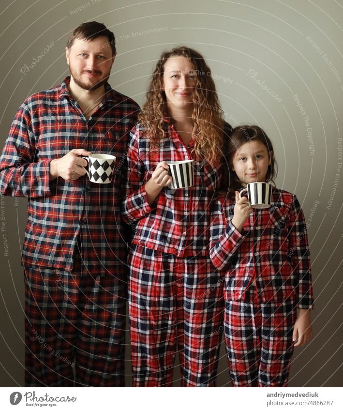 Family in pajamas on a white background. Dad, mom and little daughter with cups of tea. They smile, fool around, build funny faces and looking at camera. father's, mother's and baby's day.