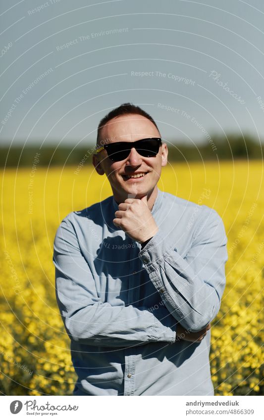 A young man in sunglasses is walking and having fun through a Sunny yellow rapeseed field, the concept of travel and freedom. summer holiday background people