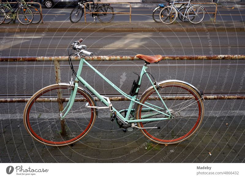 Classic ladies bike in turquoise on a rusty railing at a streetcar stop in the summer in the district of Sachsenhausen in Frankfurt am Main in Hesse change