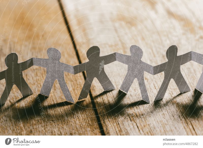 Paper People Holding Hands on a wooden table paper people team cut chain link together support friendship organization communication business group icon joined