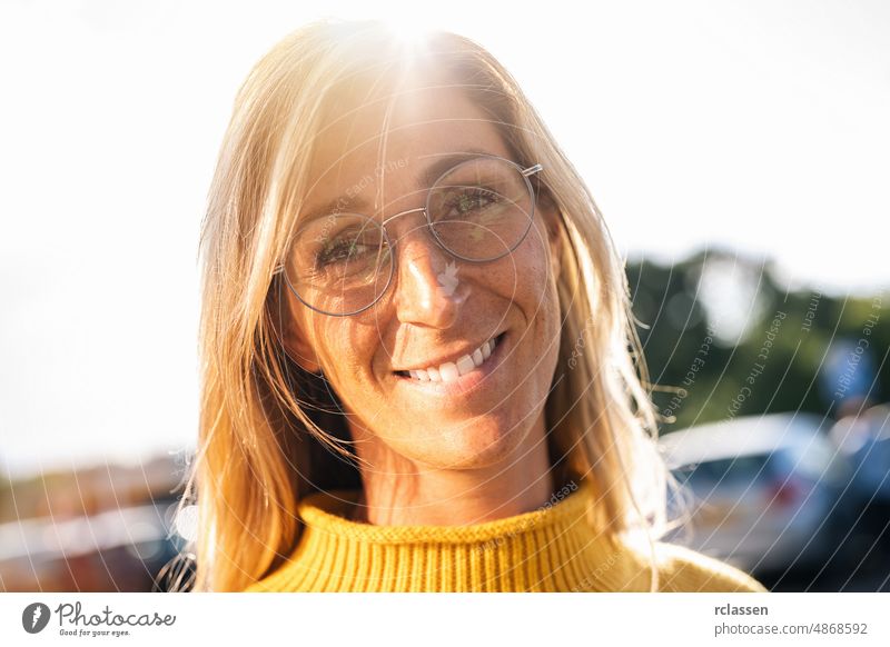 Portrait of beautiful woman smiling and looking at camera  with glasses during sunset. Outdoor portrait of a smiling girl. Happy cheerful girl laughing at city with yellow sweater.