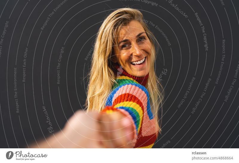 Happy excited woman pulling guy's hand wearing colorful rainbow sweater standing over black background, lgbt celebrating concept image adult attractive