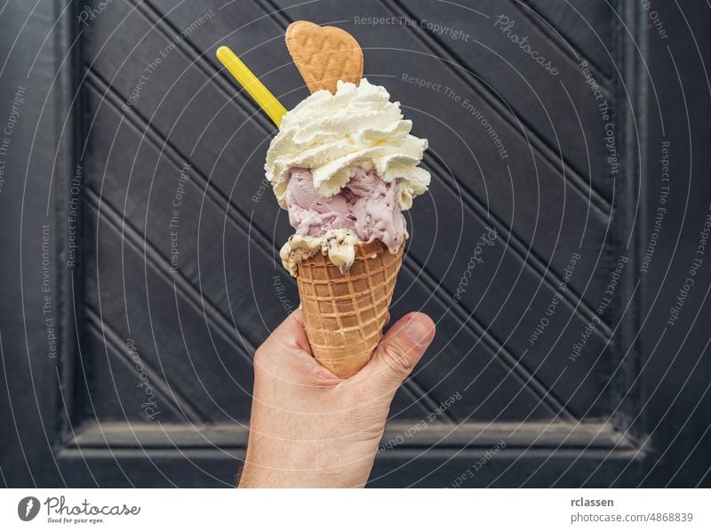 Male hand holding ice cream with cream and cookie against black doorstep. POV image summer dessert enjoyment happiness human hand lifestyles sweet food cone