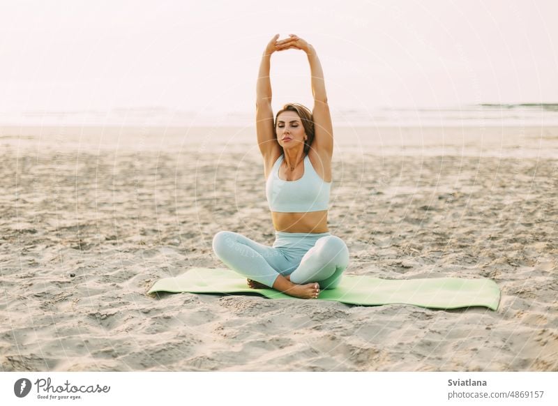 An attractive girl is sitting in a lotus position and doing exercises on the beach at sunset. The concept of a healthy active lifestyle yoga woman sea young