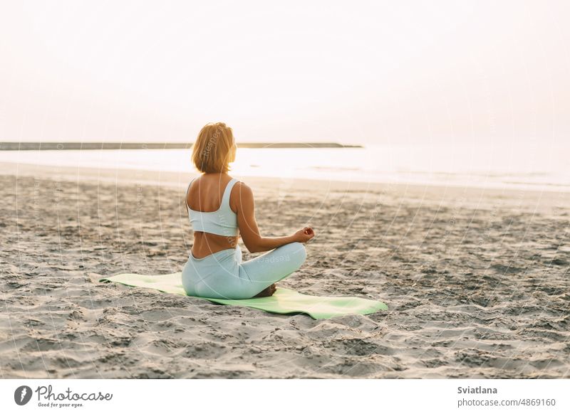 Young woman meditating in pose of lotus on beach near the sea at sunset in summer, rear view girl yoga fitness young nature sand exercise person meditation