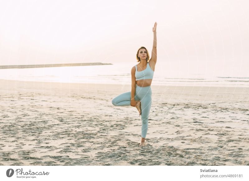 A slender girl practices yoga on the beach at sunset, performs asanas woman young beautiful summer ocean seaside holiday travel practicing vacation meditation