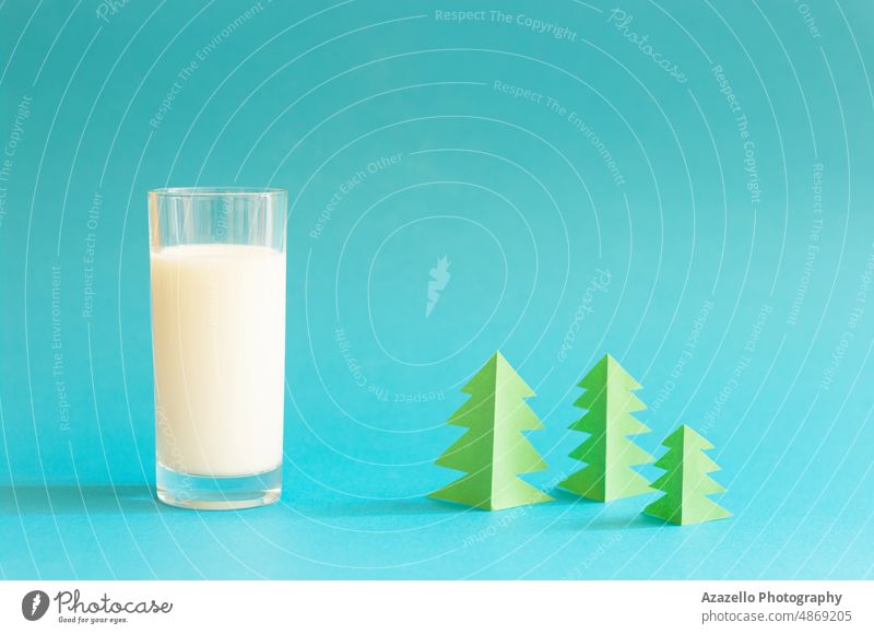 Glass of milk and green origami forest on blue background. glass tree pastel still life village nature minimalism shadow drink cow farm natural organic