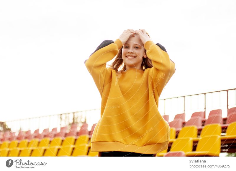 A smiling teenage girl on the background of the stands of the school stadium bleachers student studying university high school resting near young female youth