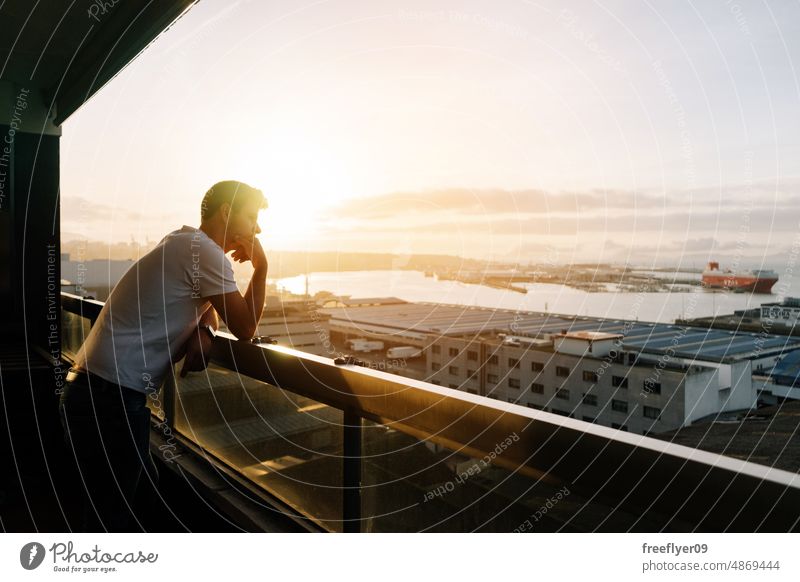Man contemplating the city from a balcony man caucasian spain landscape sea profile apartment thinking looking outside house pensive sunrise destiny unwell