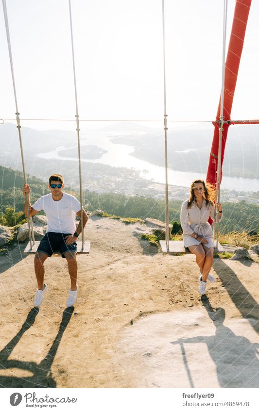 Young couple on a swing against a beautiful landscape love heterosexual nature copy space viewpoint galicia spain lifestyle vacation people travel summer fun