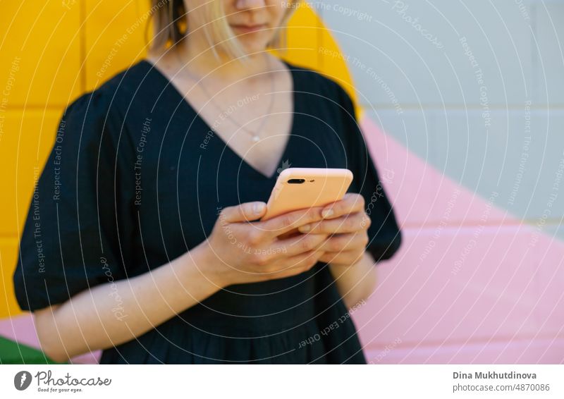 Young woman using mobile phone standing near colorful wall taking selfie or video chatting on smartphone. Screen time. Lifestyle using technology. Young remote worker employee in modern office space.