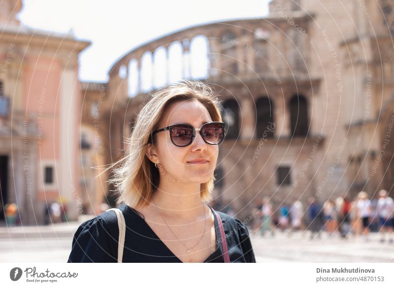 Young female tourist in sunglasses in old town admiring the view of European city on sunny day. Woman sightseeing in summer on vacation. Heatwave in Europe affecting tourists and travelers.