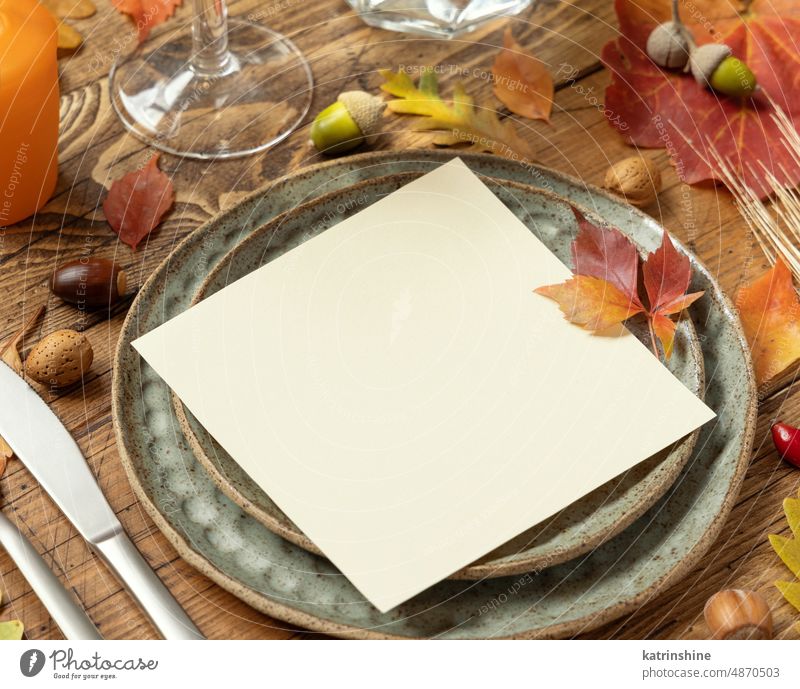 Autumn rustic  table setting with red, yellow and orange leaves, berries and blank card close up, mockup Mockup invitation Harvest wooden square acorns wheat