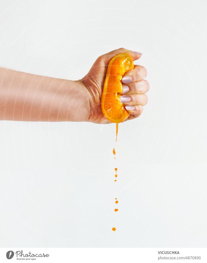 Woman hand squeezing halves of orange at white background with juice dripping. woman front view citrus fruit closeup drink drop healthy ingredient juicy liquid