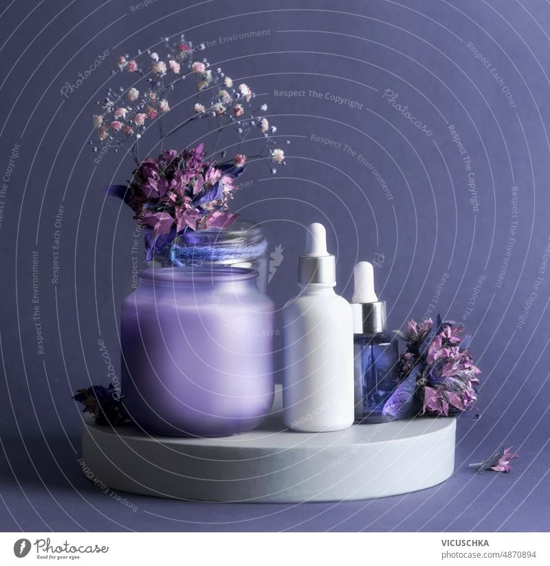 Purple beauty product setting with cosmetic serum bottles, candle and flowers. purple healthy skin care products facial beauty treatment front view copy space