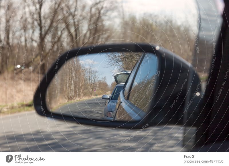 behind | is a gray car with open tailgate Landscape trees Street off vehicles cars Car two Stand stop Mirror Rear view mirror reflection Tailgate Open Road sign