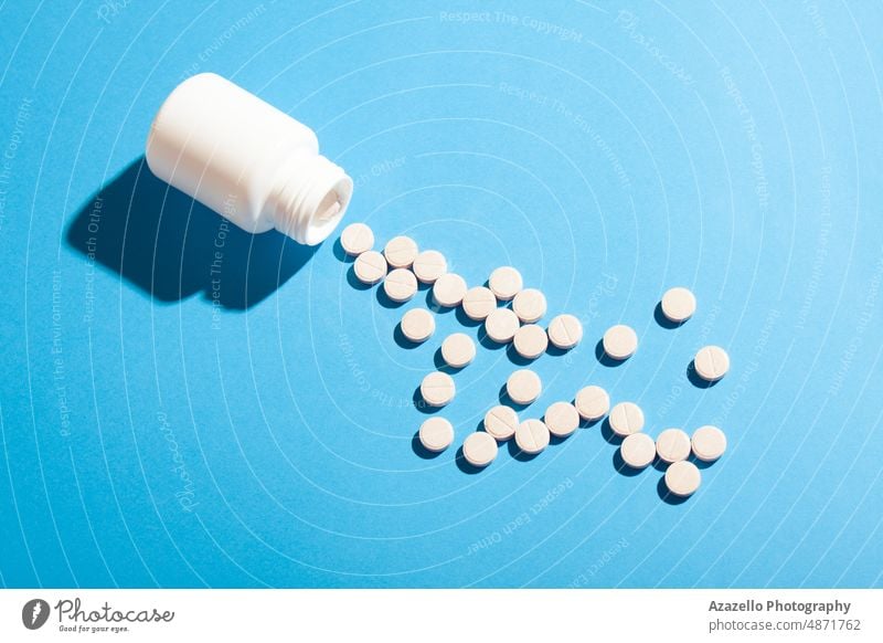 White plastic bottle and pills on blue background with hard shadow. antibiotic business capsule care chemistry clinic close up concept container corona