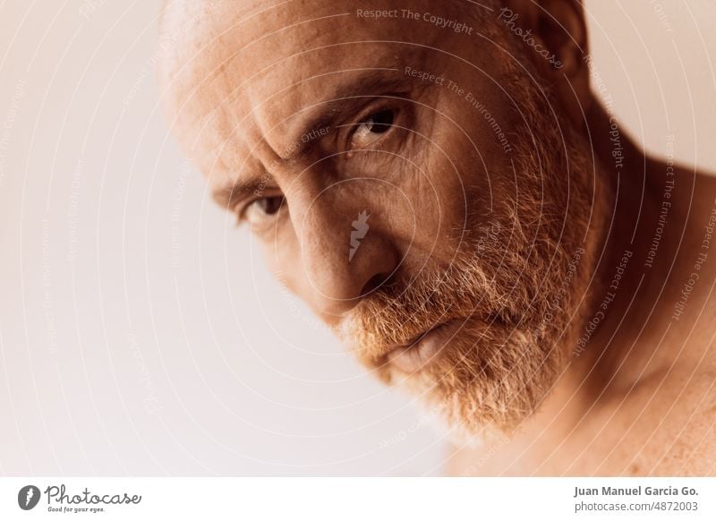 Bald man with bare torso and unkempt beard looks with serious expression, close-up and unfocused background bald naked disheveled left mustache red-haired