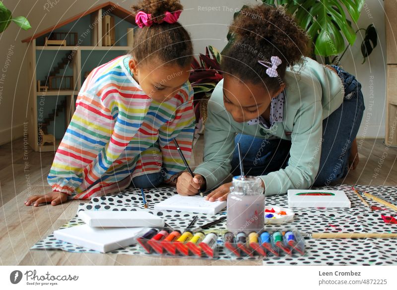 Two sibling girls of mixed race making colorful paintings and being creative in their apartment room Paint creating craft artist colour brush painter Creativity