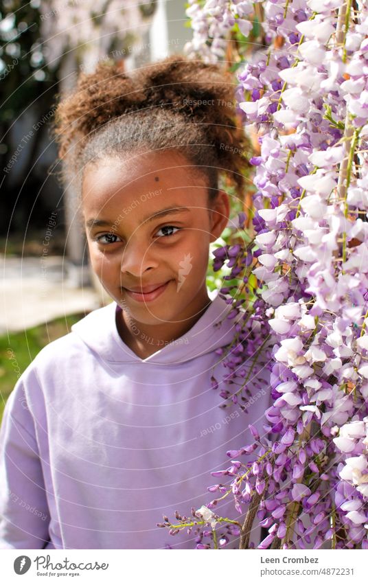 Teenage girl of mixed race with curly hair posing in between purple wisteria flowers - portrait Beauty nature summer spring teen teenager generation z Pretty