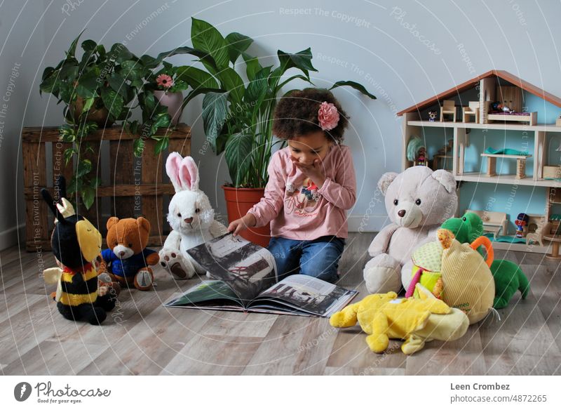 Little toddler girl of mixed race reading a story out of a book for her teddybears in het apartment room Literature books Book reading a book Reading Girl