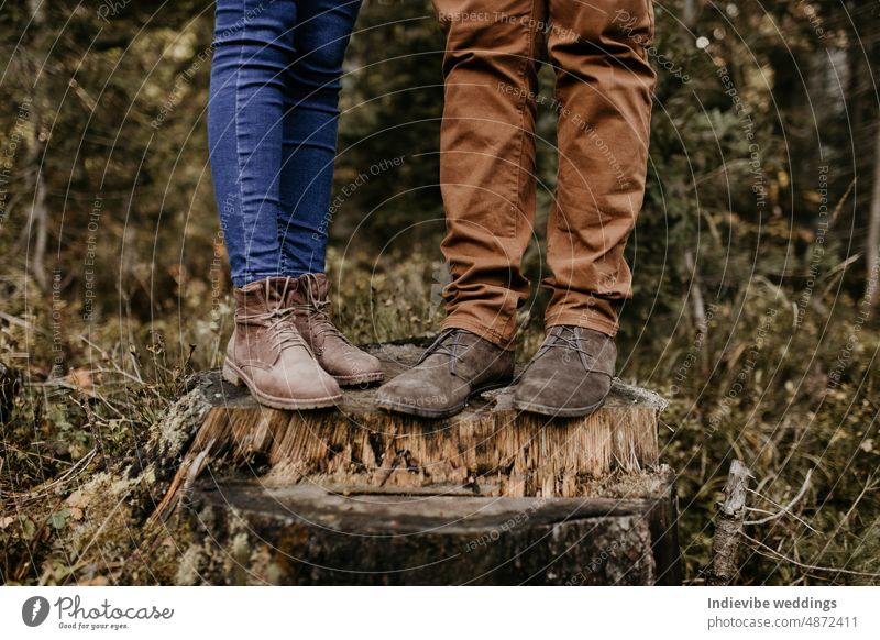 A couple is standing on a wooden trunk and their boots and jeans are on the photo. Close up shot of their trousers and brown footwear. Outdoor lifestyle in the forest.