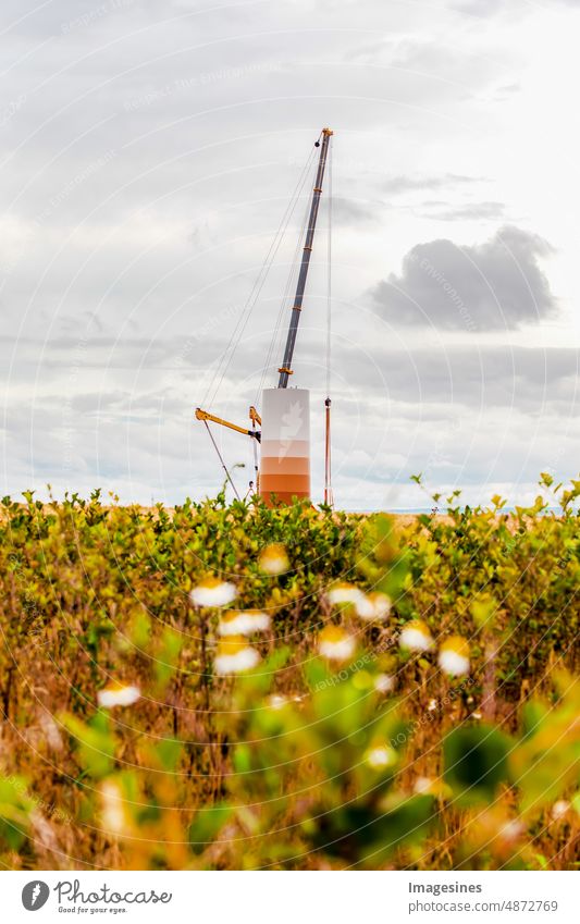 Construction and assembly of a wind turbine by crane on a construction site. Farmland with construction work on wind farm in Germany. Energy saving concept from wind turbine construction with cloud sky