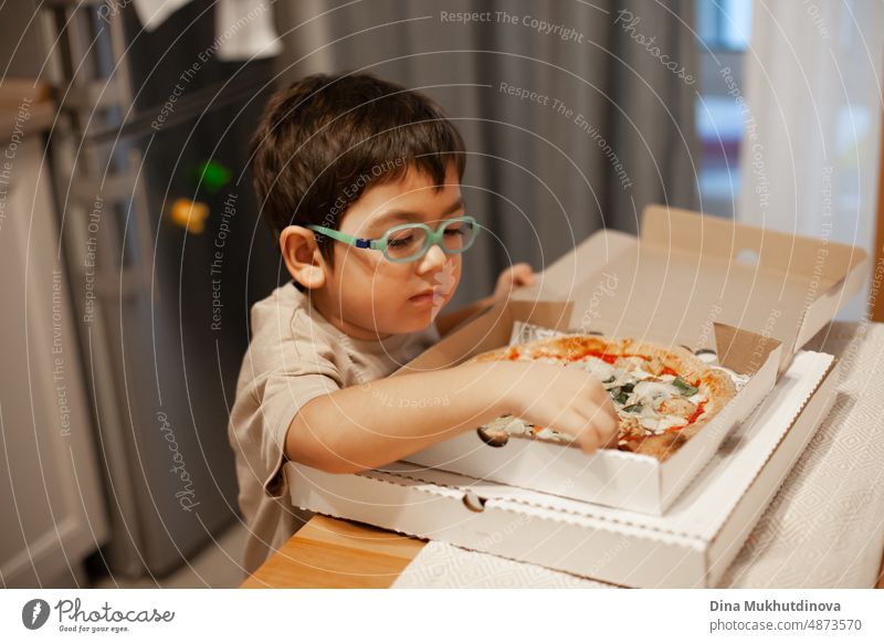 Kid of 5 years old eating pizza from carton box at home. Pizza delivery making people happy. Enjoying food at home. Boy wearing glasses with pizza. childhood