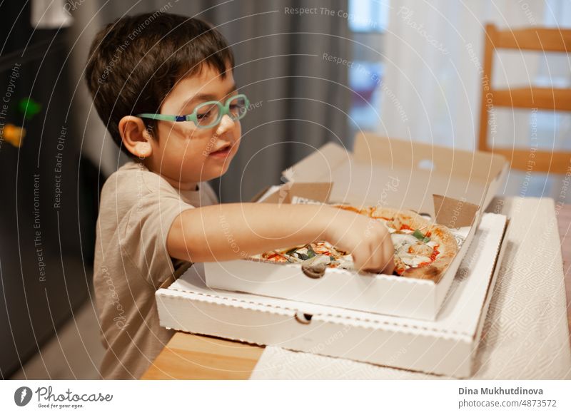 Kid of 5 years old eating pizza from carton box at home. Pizza delivery making people happy. Enjoying food at home. Boy wearing glasses with pizza. childhood