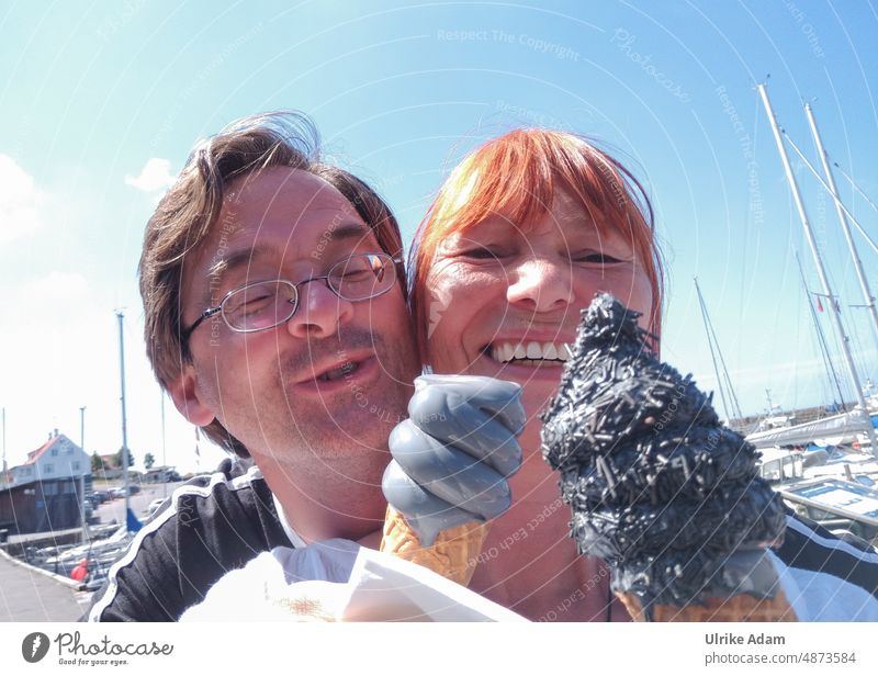 Delicious licorice ice cream |Happy couple with ice cream in hand looks joyfully at the camera. In the background you can see a harbor in nice weather. Ice