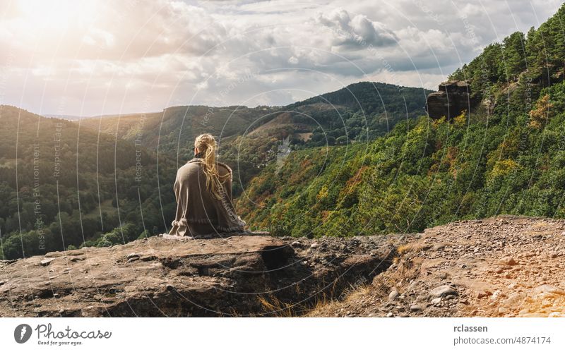 Traveler explorer young woman sitting on rocky stone and looking at mountain valley in autum, rear view. adventure adult blond people thunking relax beautiful