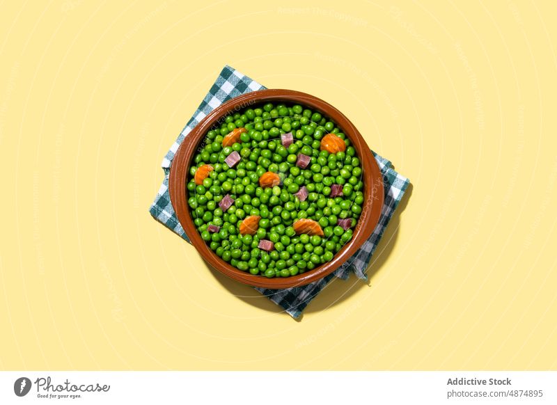 Green peas with serrano ham and carrot on yellow background green vegetable healthy mix dinner food lunch spanish cooked colorful bright bowl organic natural