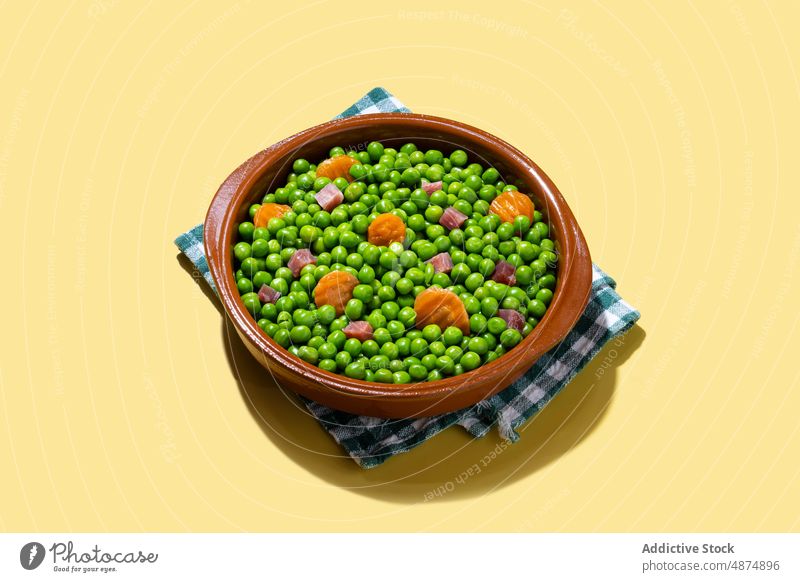 Green peas with serrano ham and carrot on yellow background green vegetable healthy mix dinner food lunch spanish cooked colorful bright bowl organic natural