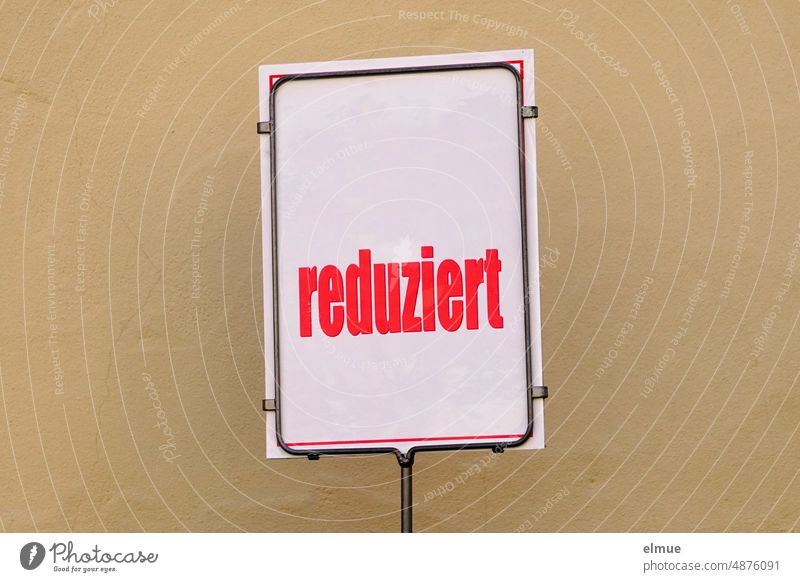 white sign with bright red inscription - reduced - in front of beige house wall / special offer / catching customers Reduced ssv sale Trade red prices Summer