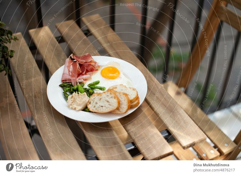 Breakfast with egg, meat jamon, spinach and bread on terrace wooden table. Delicious homemade breakfast on balcony. tasty food nutrition easter eating natural