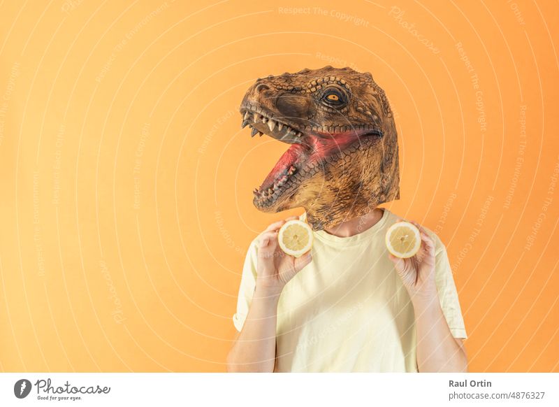 Woman in dinosaur head mask holding fresh lemon slices on orange background person vitamin unrecognizable fruit healthy healthy food animal mask surreal