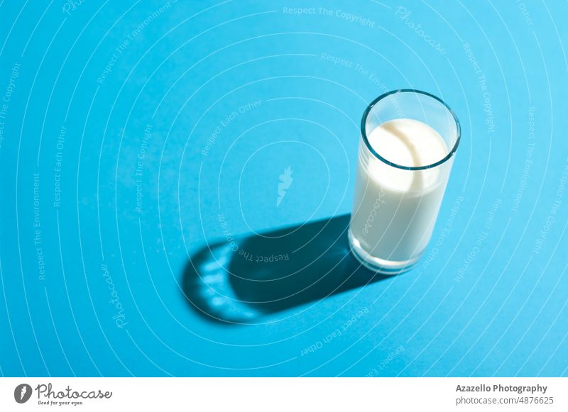 Glass of milk under the bright light with hard shadow on blue backgorund. Milk glass pastel still life minimalism abstract healthcare baby background beverage