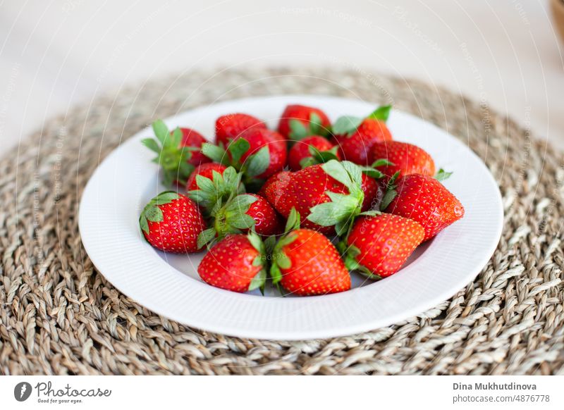 Fresh organic red strawberries on white plate and jute placemat on the table ready for breakfast. Delicious freshly collected berries, sustainable gardening. Growing strawberries in the garden or in the apartment.