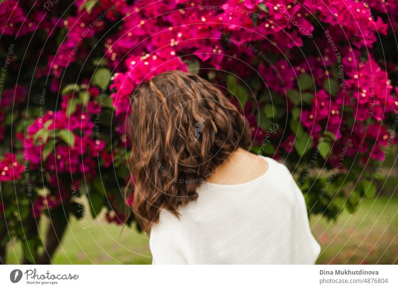Woman brunette dancing near pink flowers on tree in summer. Beautiful happy woman in the park or garden with blooming trees. hairstyle beautiful background