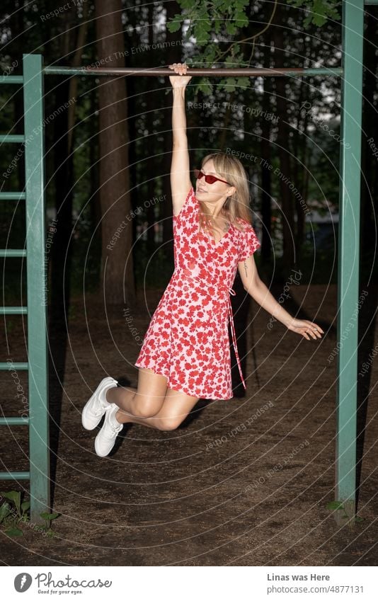 A strong and beautiful girl in a red dress is having some fun in the woods. With her fashionable sunglasses and white sneakers, she is most definitely the queen of a forest. Summer nights with some wild action.
