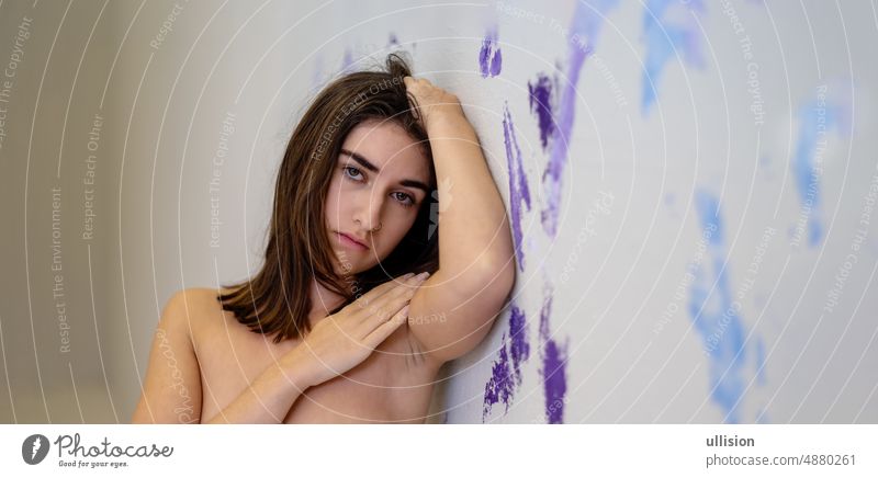 Portrait of a young sexy seductive brunette woman standing at the purple, violet, blue artistic painted studio wall background copy space view presentation