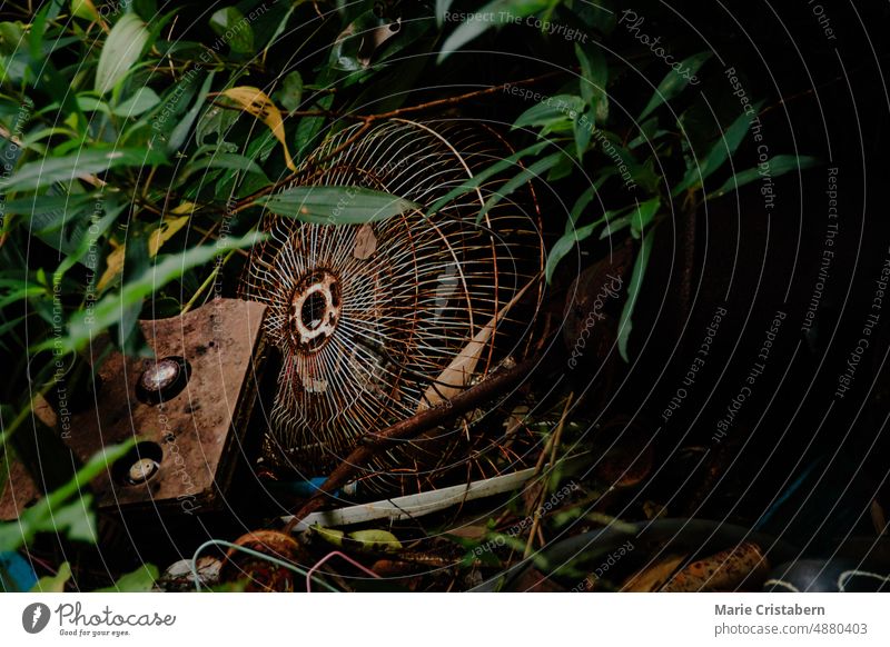Old rusty discarded electric fan in a garbage pit being overran by thick foliage environment concept ecology reclaimed by nature earth day overgrown lush