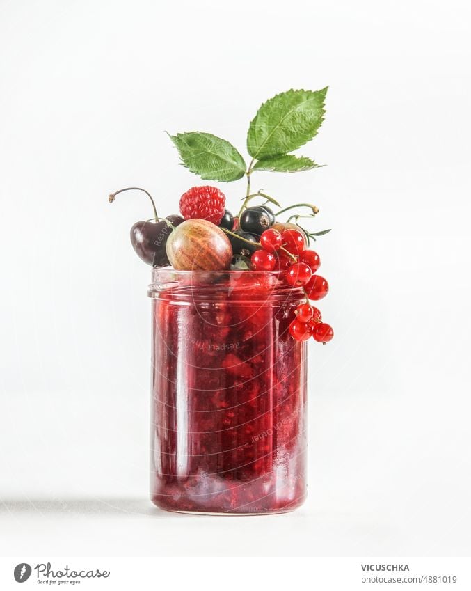 Red jam in jar with various berries at white background. Preserving of delicious summer fruits. red red currants raspberry cherry black currants gooseberry