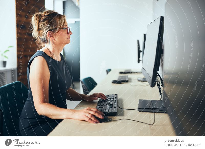 Concerned businesswoman working on computer in office. Busy woman sitting at desk at front of computer monitor. Focusing on work. Open office. Copy space right
